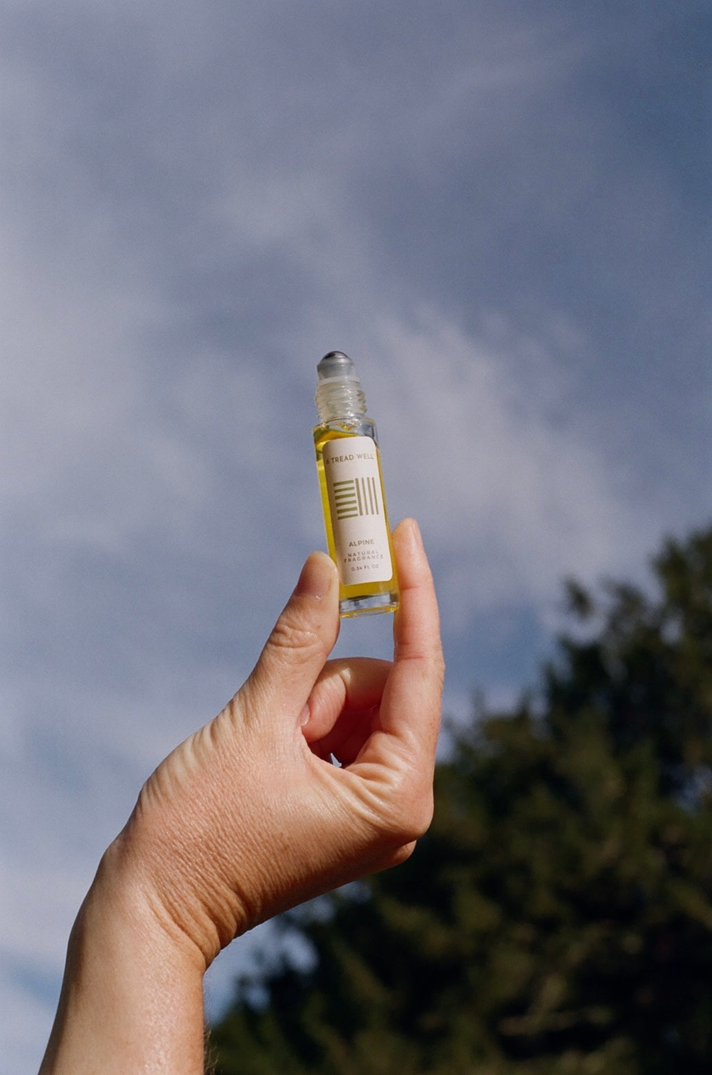 Hand holding a small bottle with a label against a cloudy sky