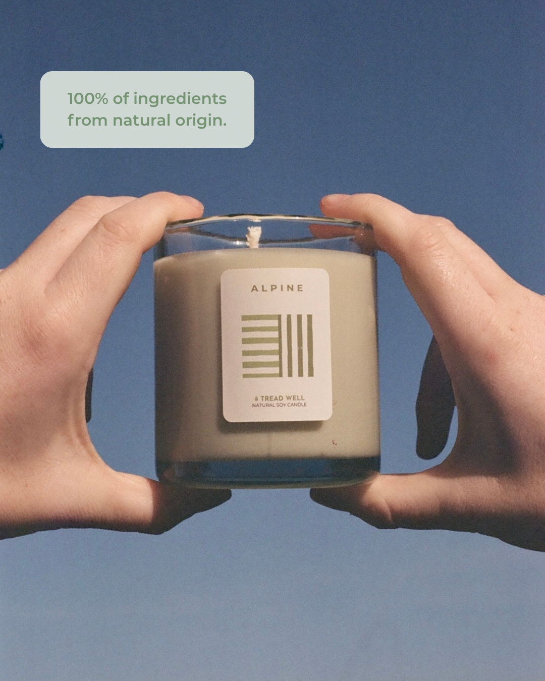 Two hands holding a candle labeled 'Alpine' against a blue background with text about natural ingredients.