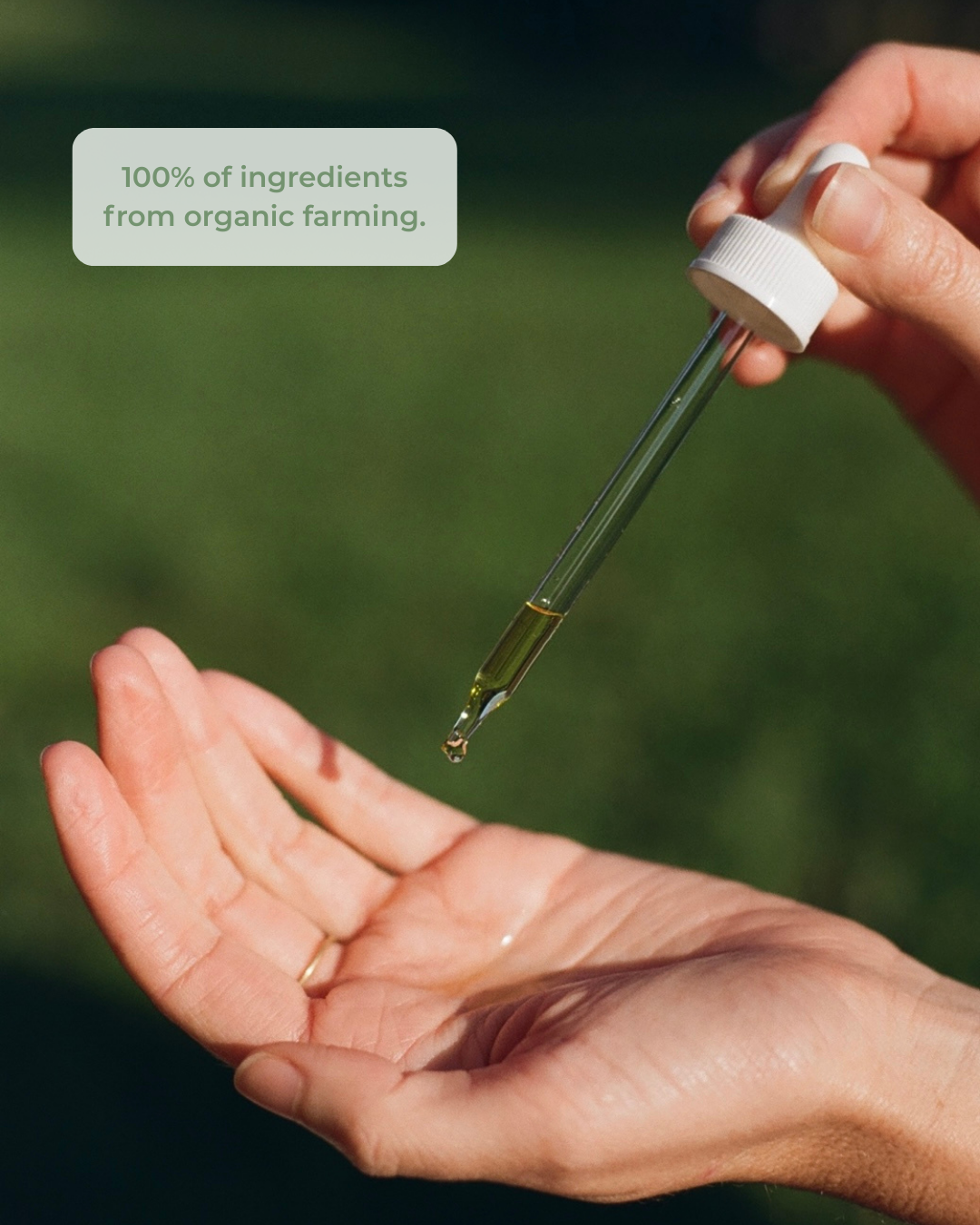 Hand holding a dropper with green liquid over an open palm against a blurred green background, emphasizing organic ingredients.