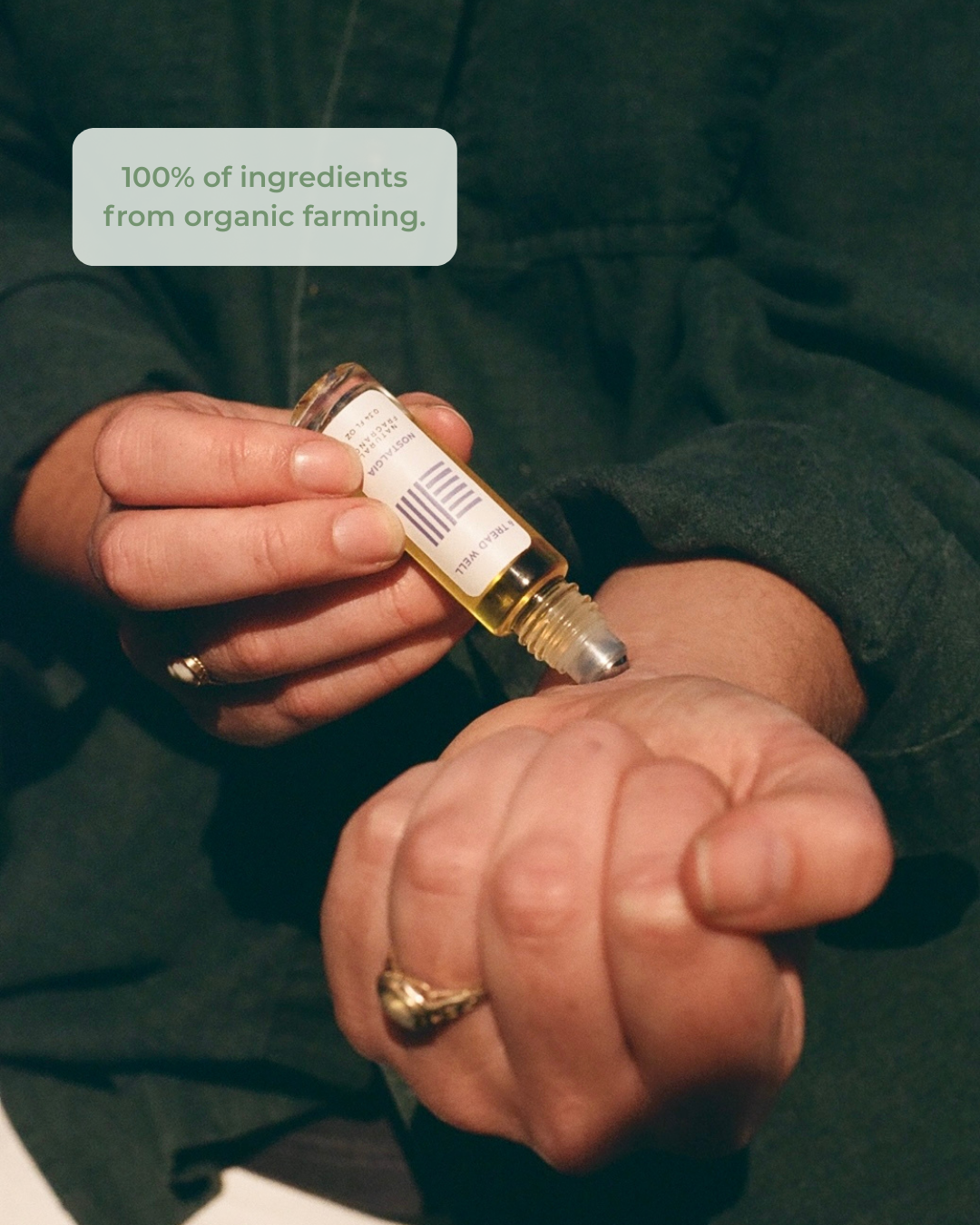 Person holding a dropper bottle of "nostalgia" fragrance with a label, wearing a dark green shirt and text indicating natural ingredients