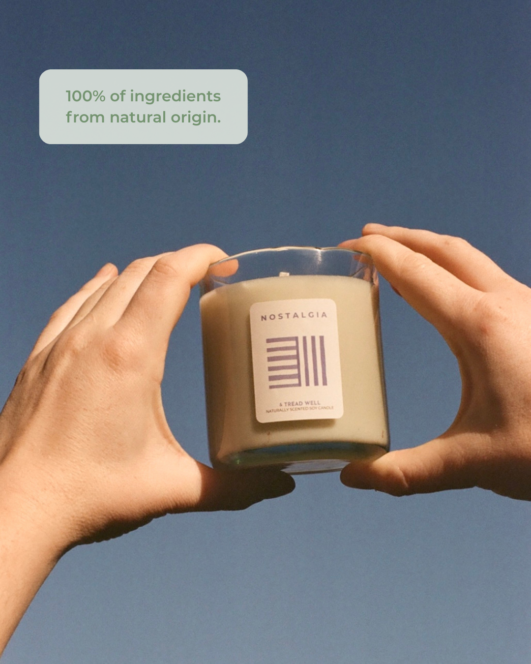 Two hands holding a candle labeled 'Nostalgia' against a blue background with text about natural ingredients.