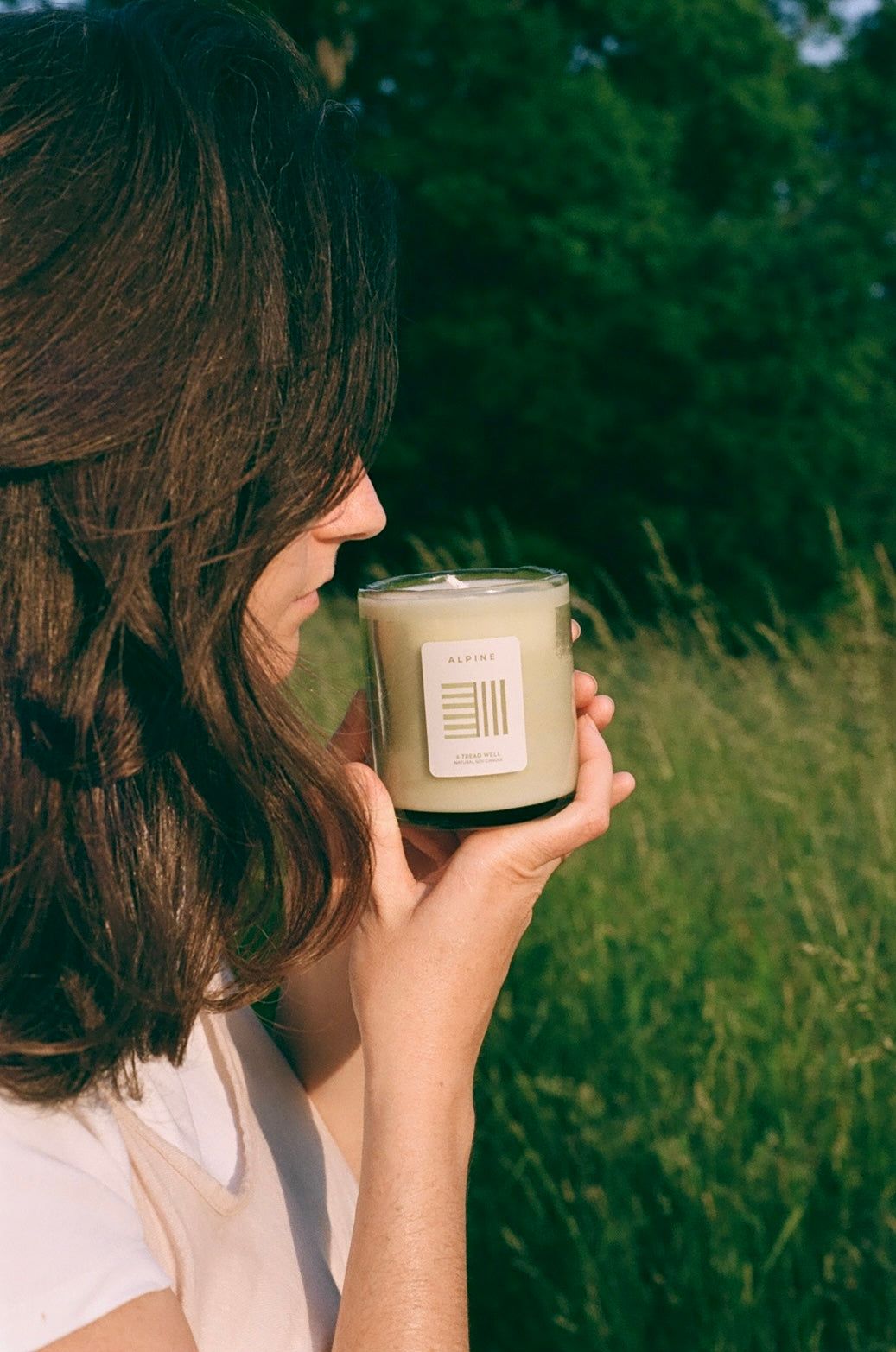 Person holding a candle in a natural setting with greenery