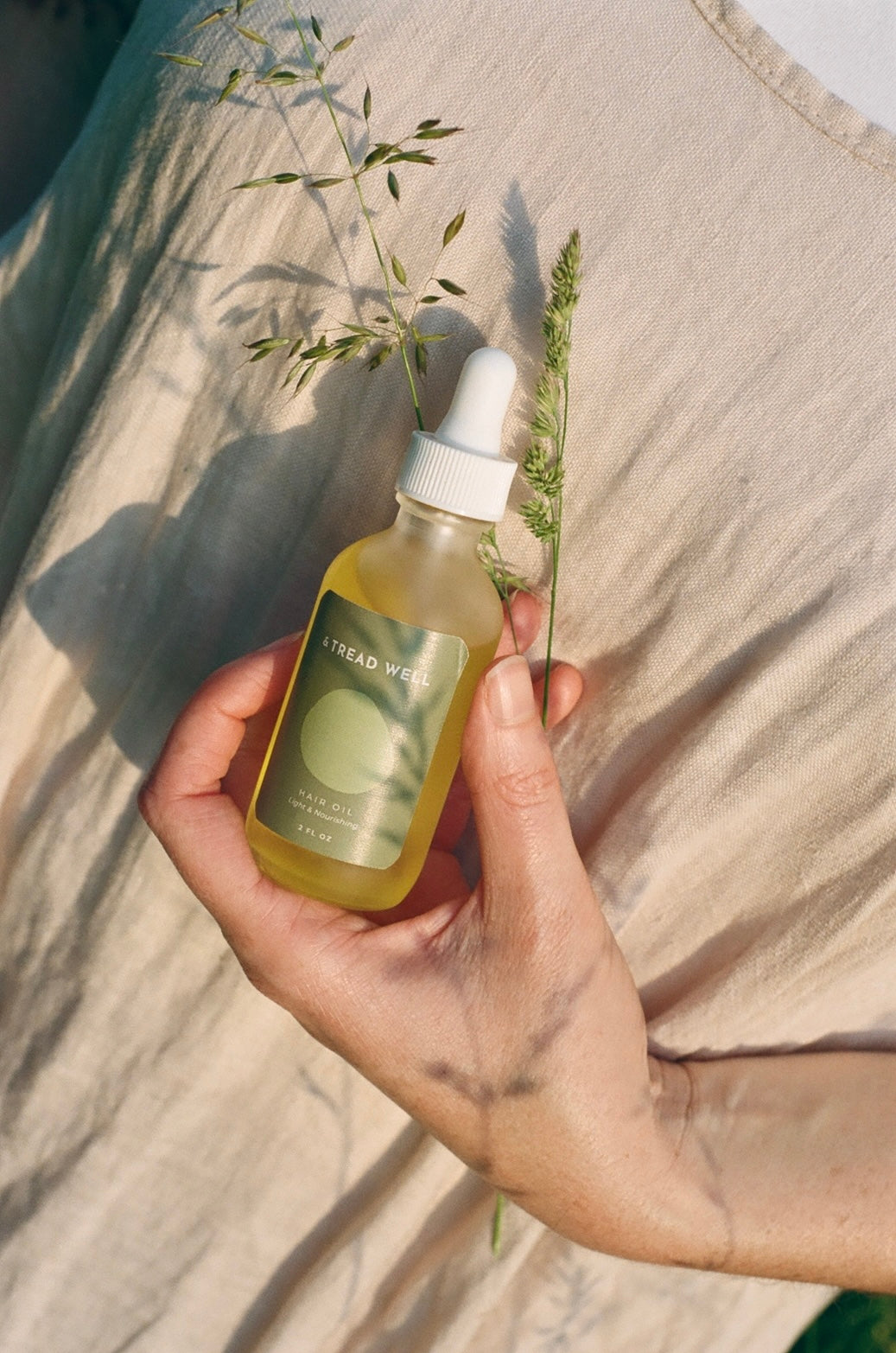 Hand holding a dropper bottle of hair oil product with a natural background
