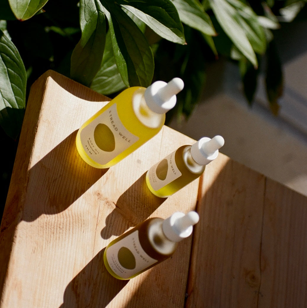 Three bottles with droppers on a wooden surface with green leaves in the background