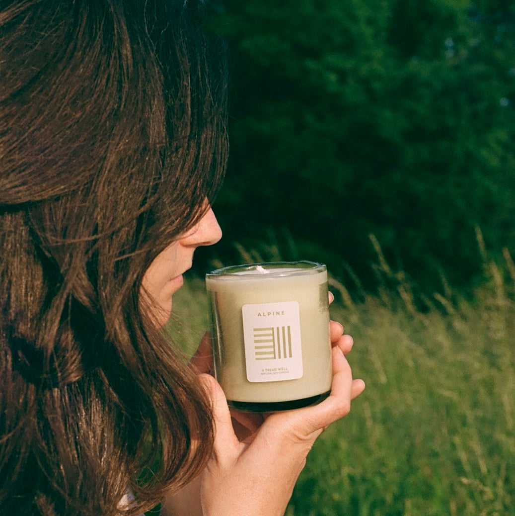 Person holding a candle in a natural setting with greenery