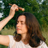 Woman in a field holding a stick and a small container, surrounded by greenery.
