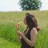 Woman smelling fragrance in a grassy field with trees in the background