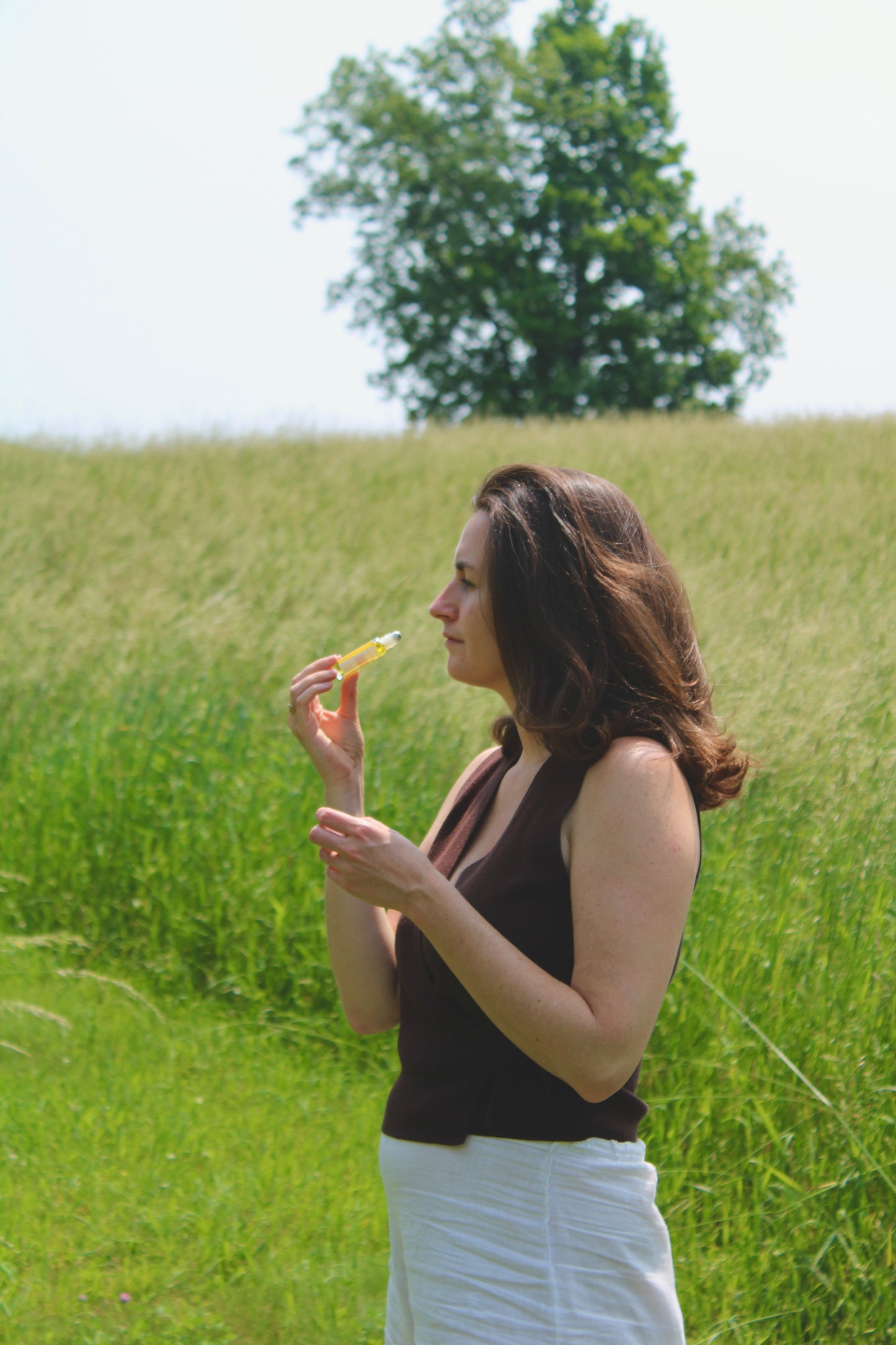 Woman smelling fragrance in a grassy field with trees in the background