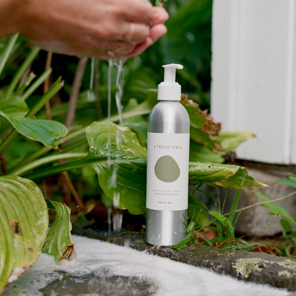 Bottle of soap with a pump being held over water, surrounded by greenery