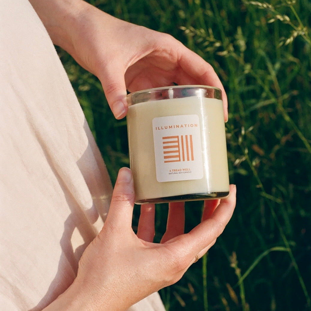 Hand holding a candle labeled 'Harmony' against a natural background