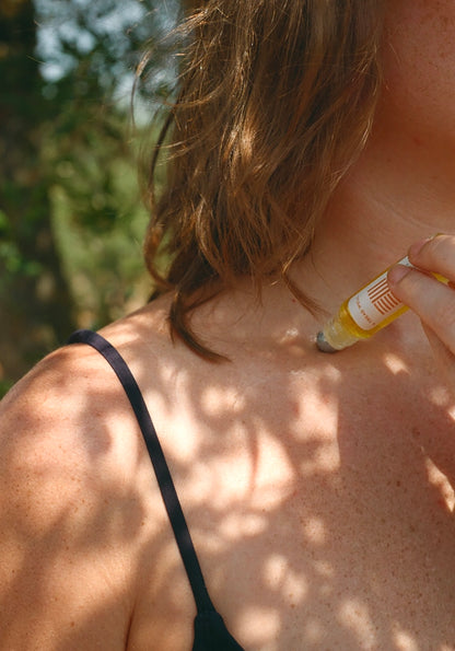 Person applying a rollerball fragrance their collar bone outdoors