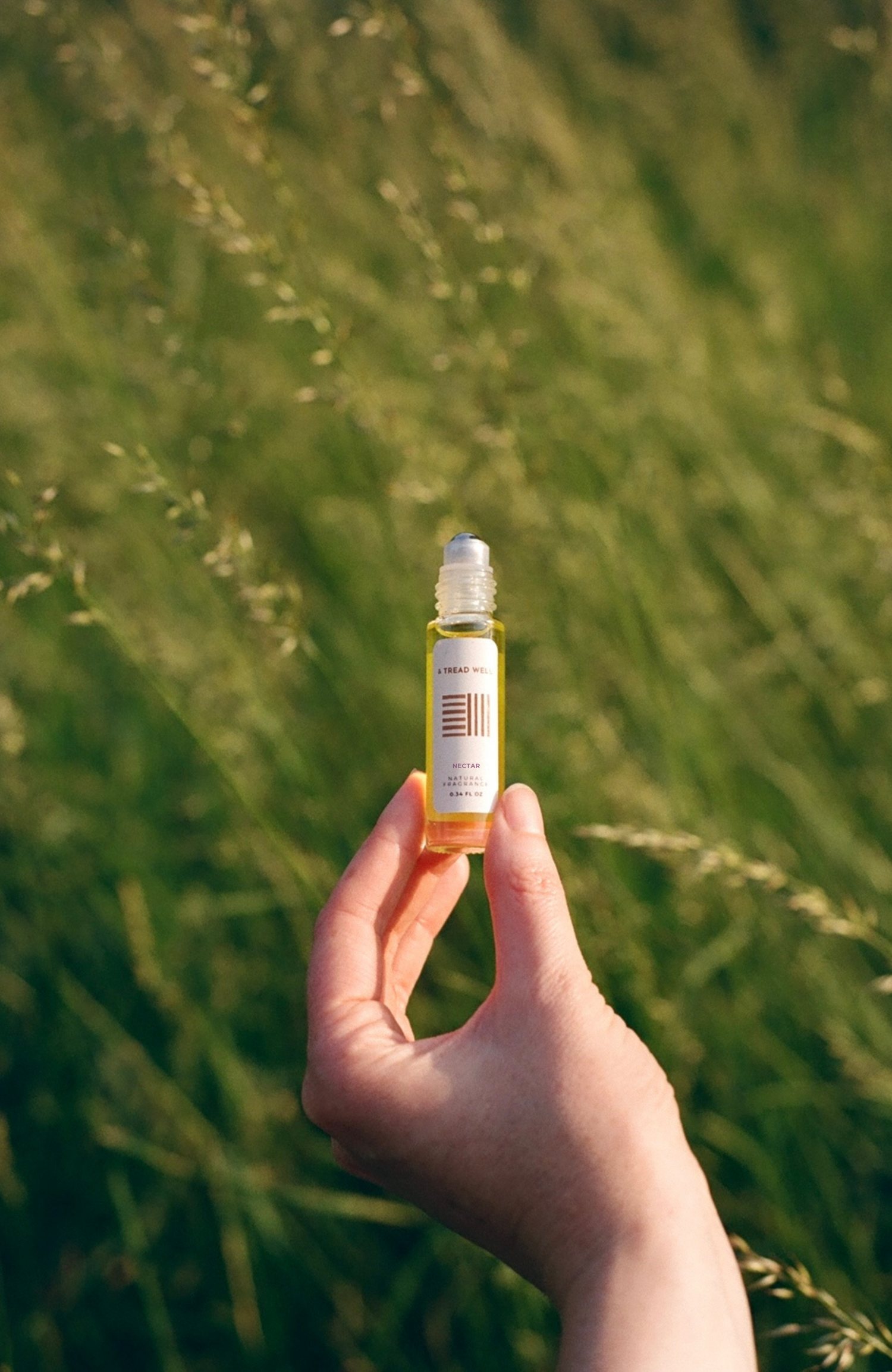 Hand holding a small bottle of fragrance with a green field in the background