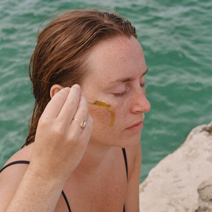 Woman applying oil cleanser on her face by the sea.