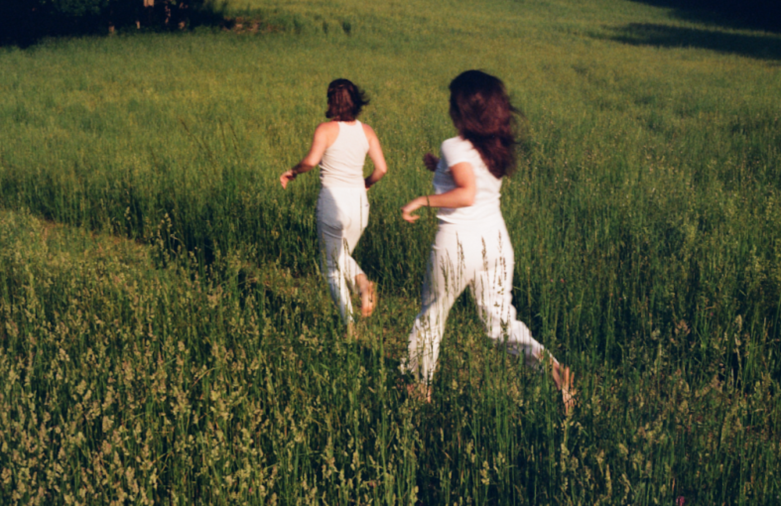 Two girls dressed in white running through a green field.