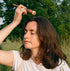 Woman in a field holding a stick and a small container, surrounded by greenery.