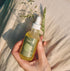 Hand holding a dropper bottle of hair oil product with a natural background