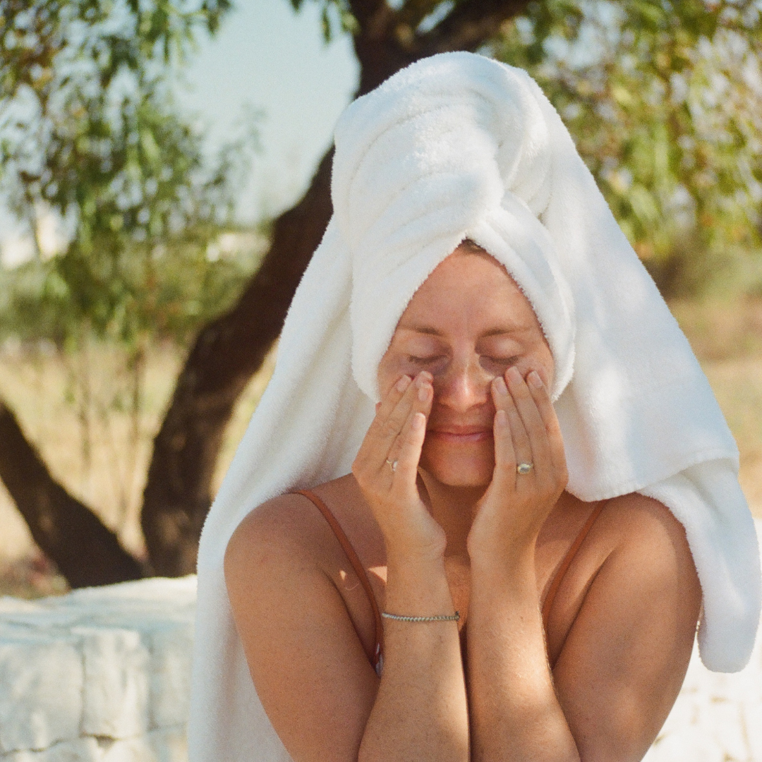 Woman with a white towel on her head outdoors, surrounded by greenery.