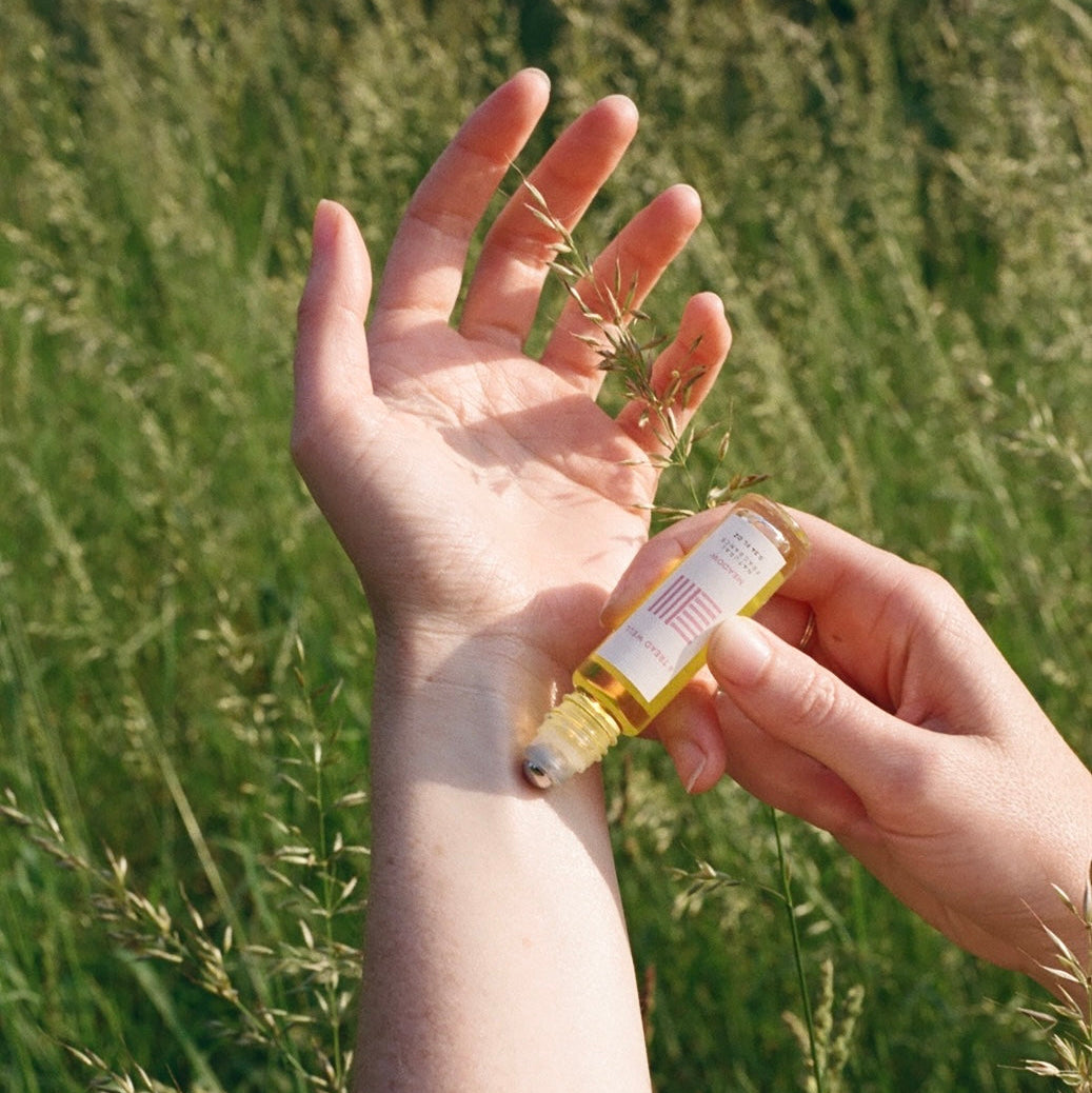 Person applying a small bottle of oil to their hand against a grassy background