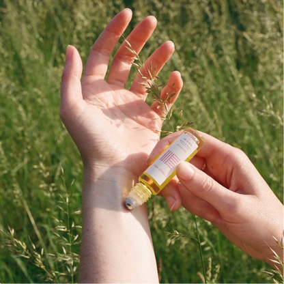 Person applying a fragrance oil to their wrist in a grassy field.