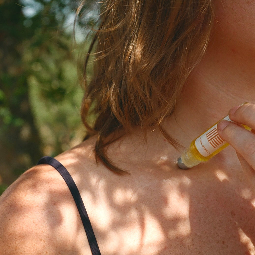 Person applying a rollerball fragrance their collar bone outdoors
